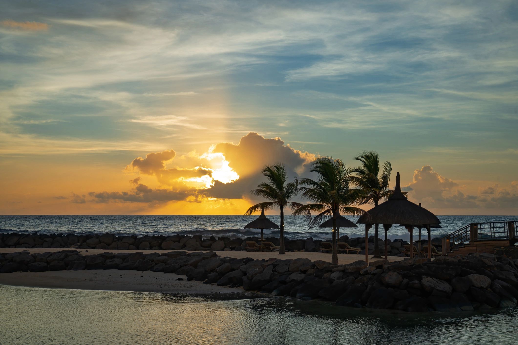 Sunset over a rocky tropical shoreline with calm ocean